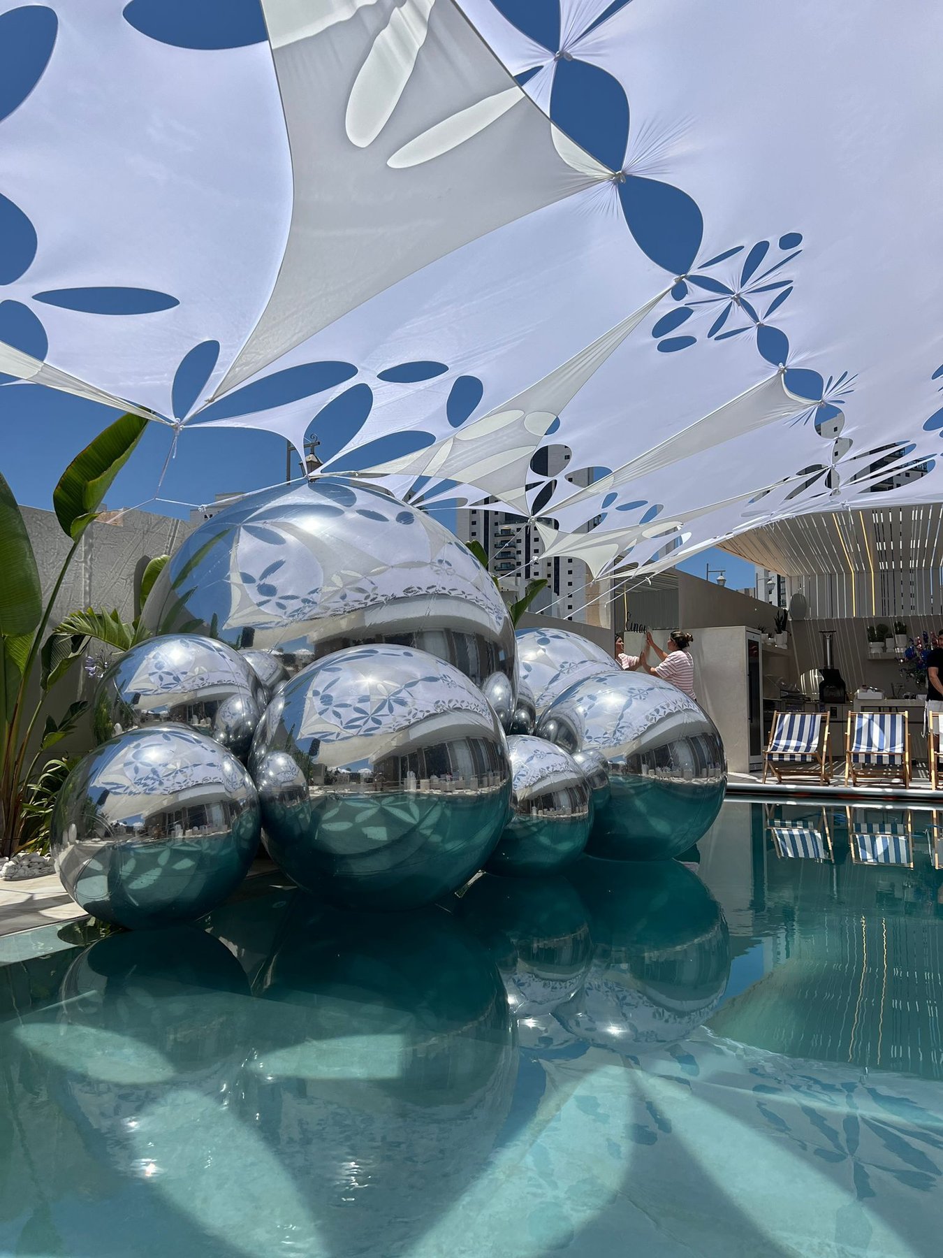 Composition de ballons miroirs argentés au bord d’une piscine sous des voiles décoratives