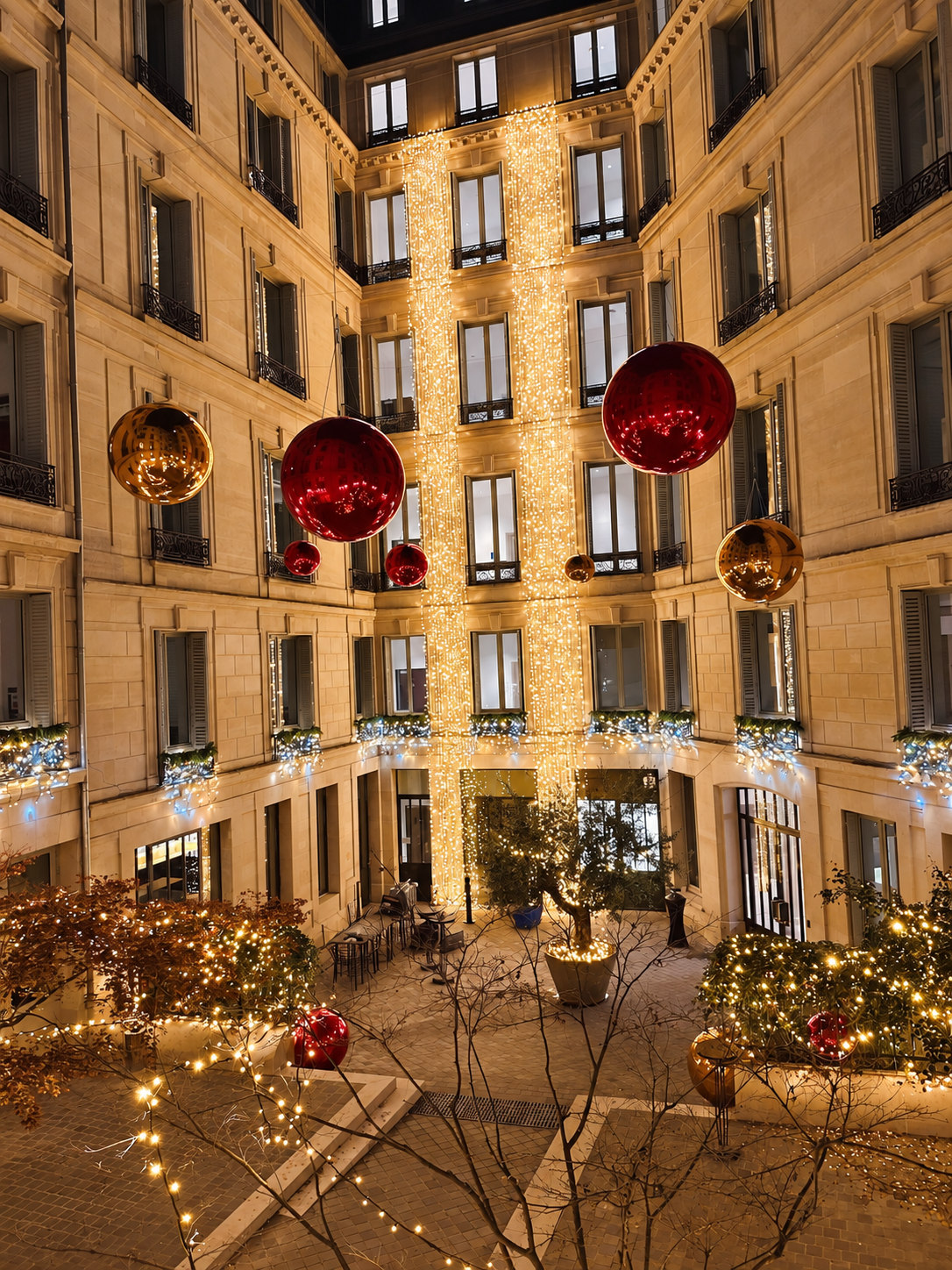 Ballons miroirs rouges et dorés suspendus dans une cour illuminée
